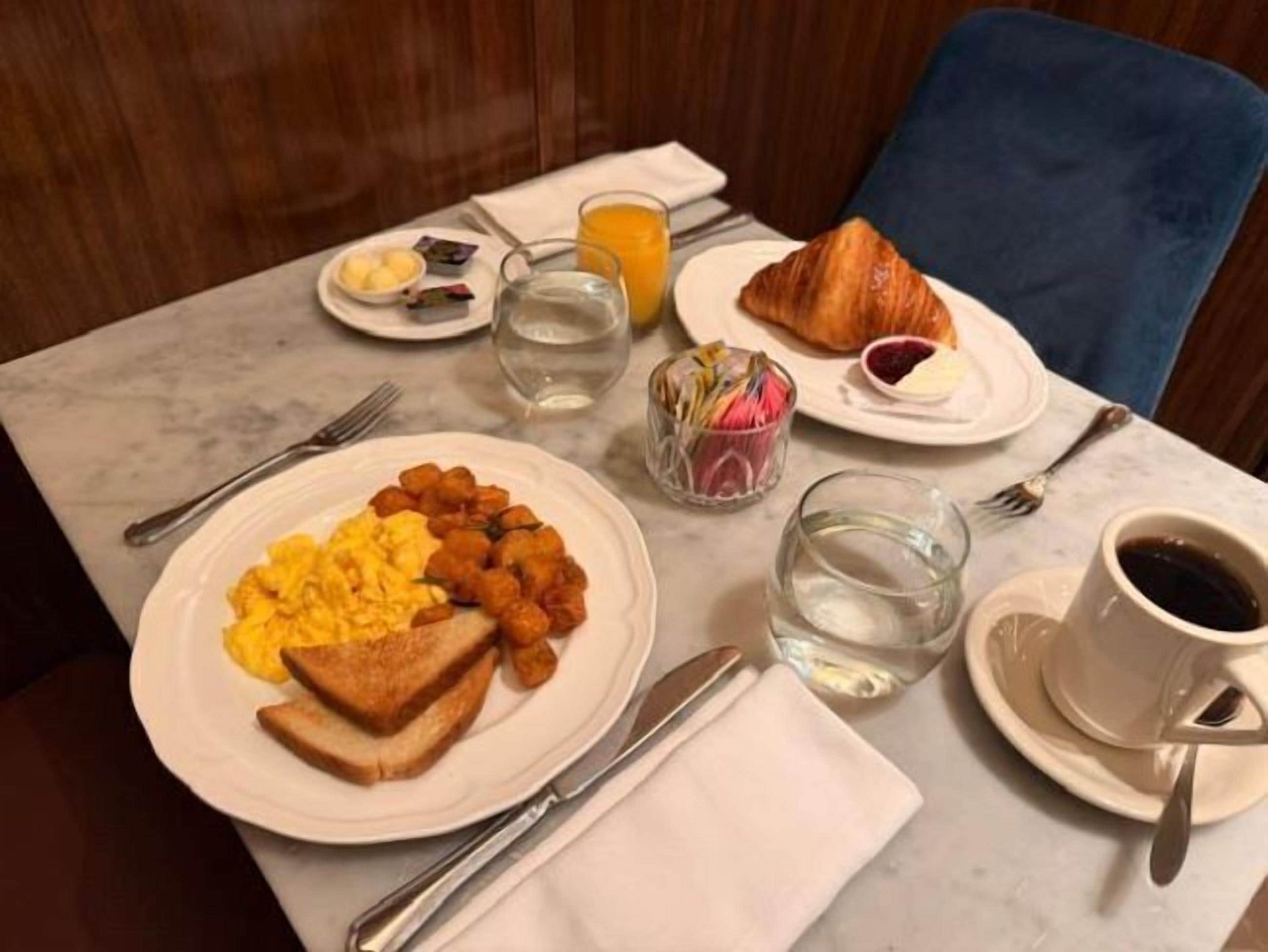 Une table de petit-déjeuner avec des assiettes contenant des œufs brouillés, des toasts, des croissants et du jus de fruits.