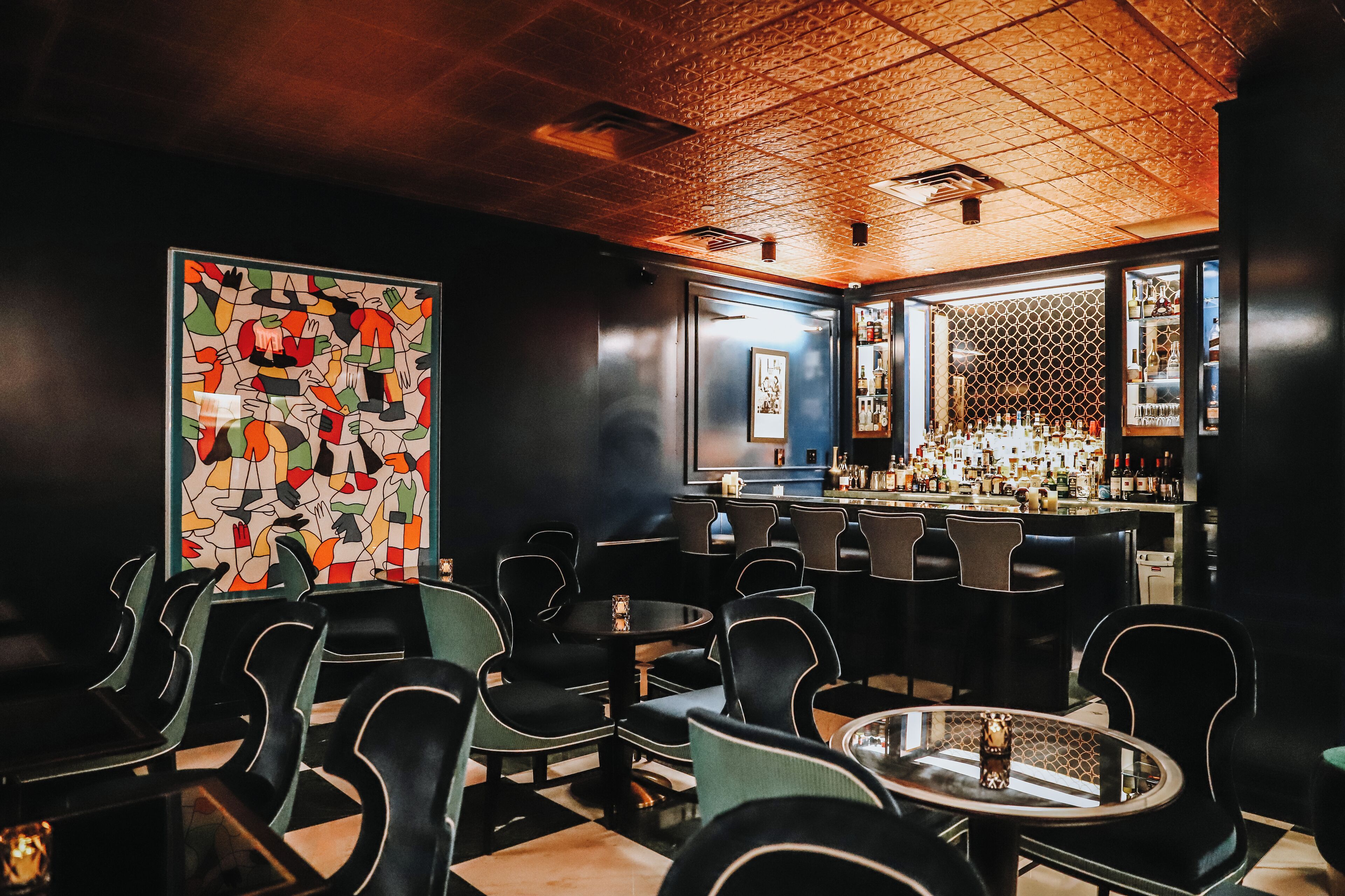 Un espace bar avec un plafond à motifs, des chaises noires et vertes, et un comptoir où sont exposées des bouteilles.