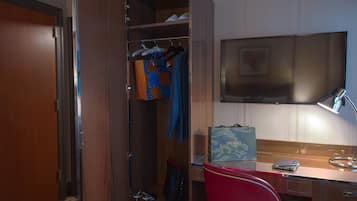 A hotel room with a wooden wardrobe, a desk with a laptop, a red chair, and a television on the wall.