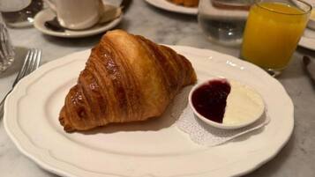 Un croissant sobre un plato con un recipiente pequeño de mermelada y un vaso de zumo de naranja.