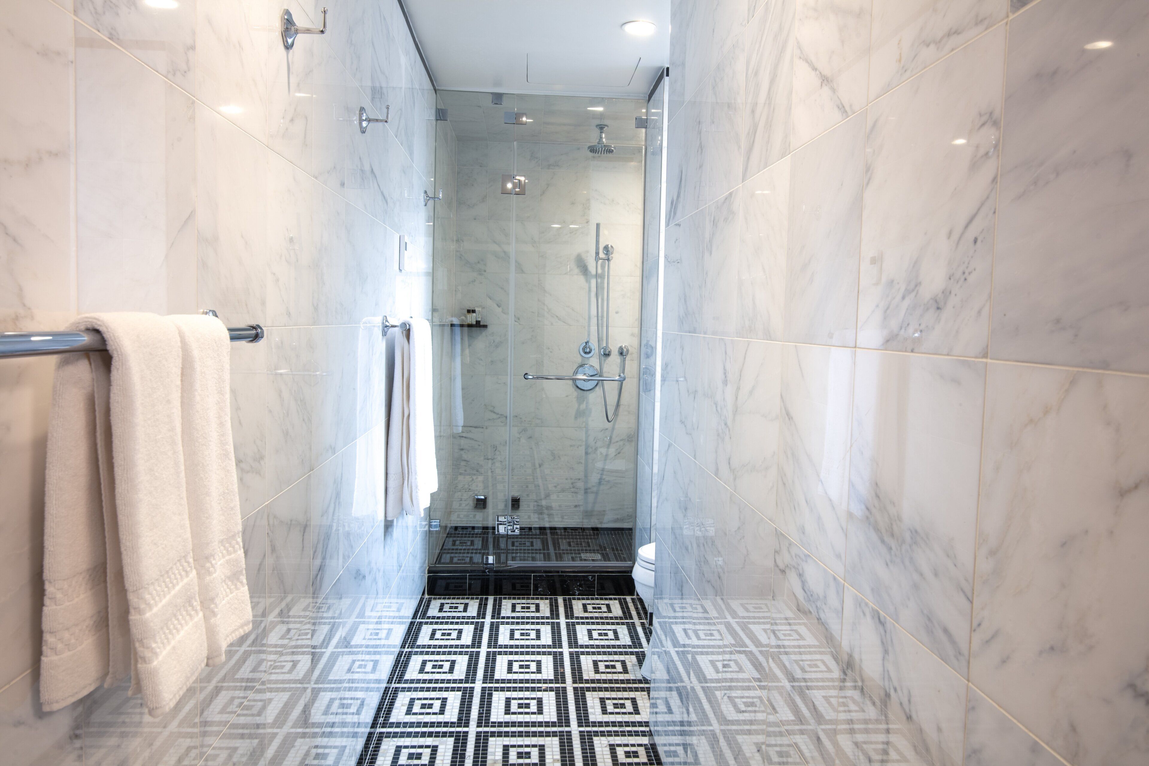 A modern bathroom with a glass-enclosed shower, a patterned floor, and a towel rack.