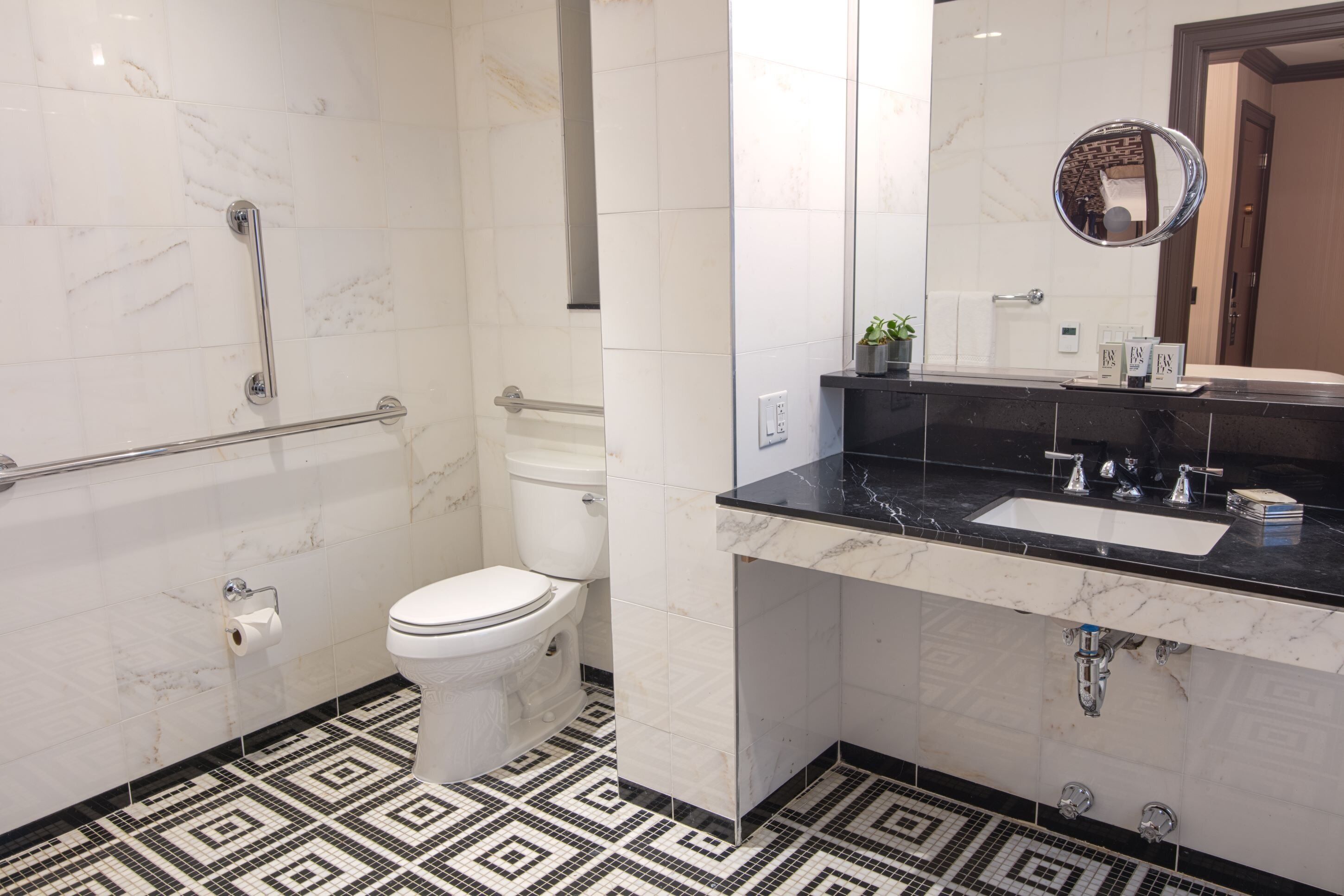 A bathroom with a toilet, a shower with a grab bar, a sink with a mirror, and a patterned floor.