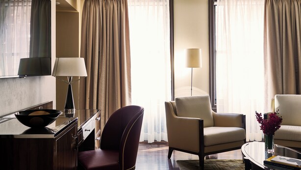 A hotel room with a desk, two chairs, a lamp, and a vase with flowers.