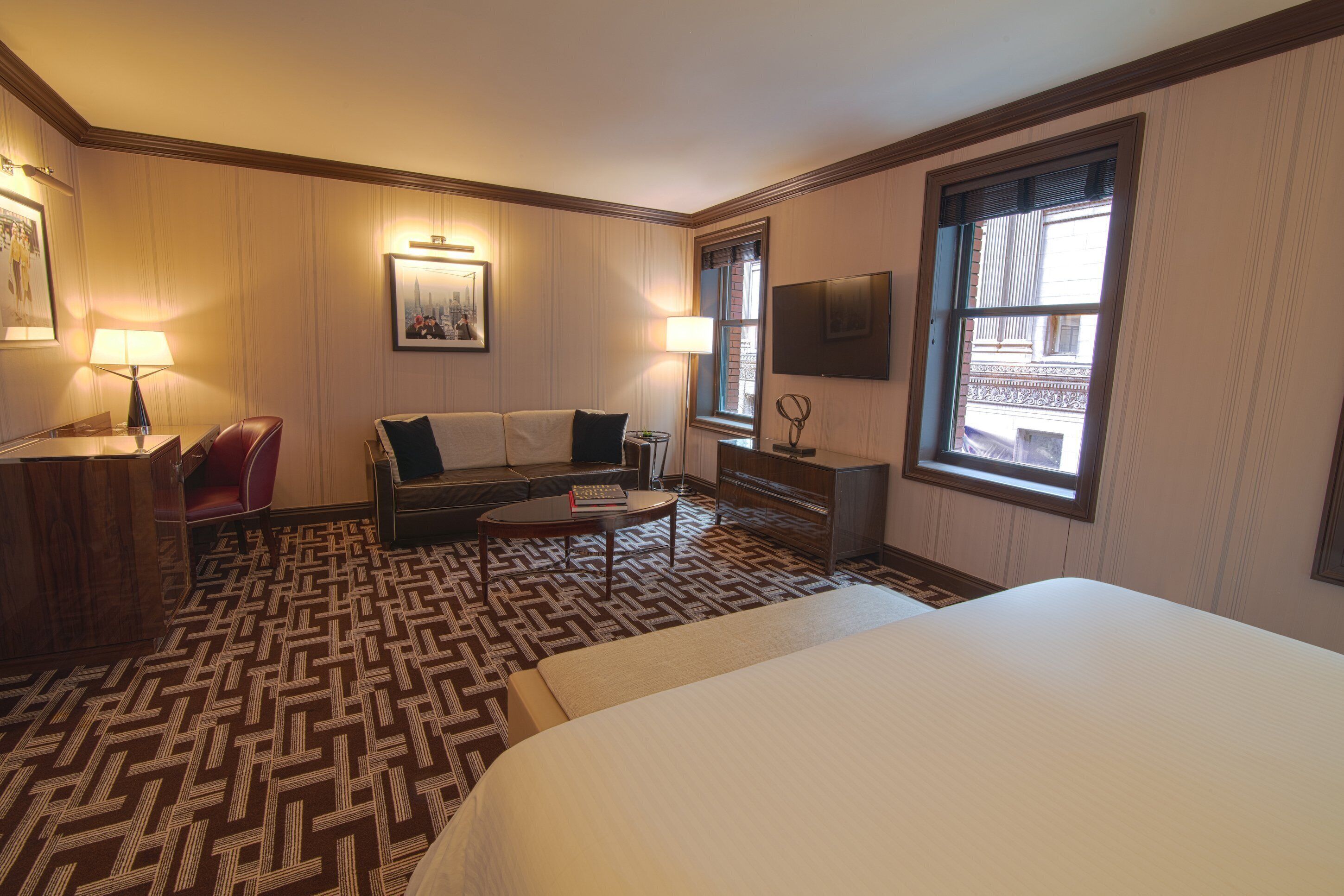 Une chambre d’hôtel avec un grand lit, un canapé, une petite table, un bureau et une fenêtre donnant sur des immeubles.