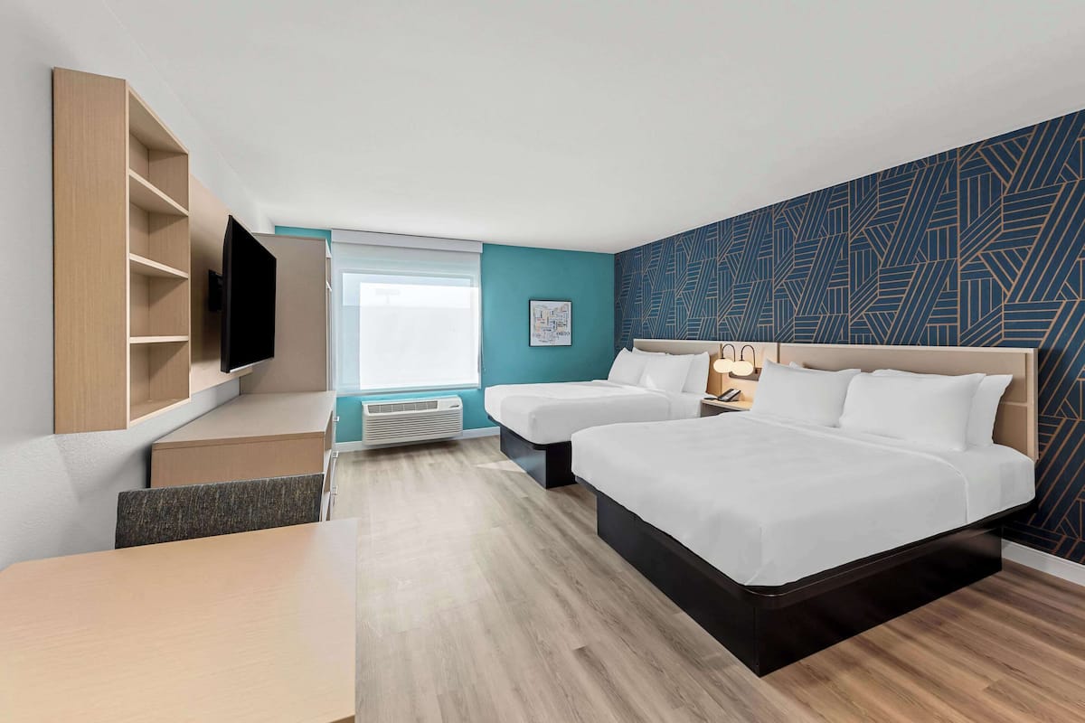 A hotel room with two beds, a TV, a desk, and a window.