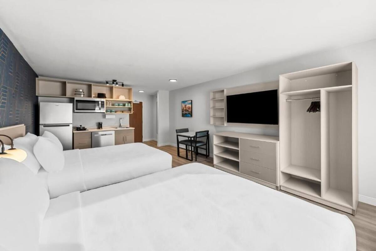 A modern hotel room with a bed, kitchenette, TV, and wardrobe.