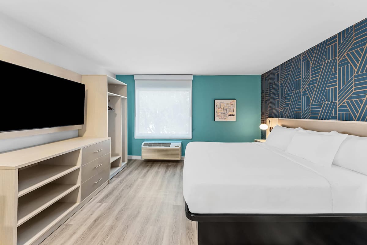 A hotel room with a bed, a TV, a wardrobe, and a window.
