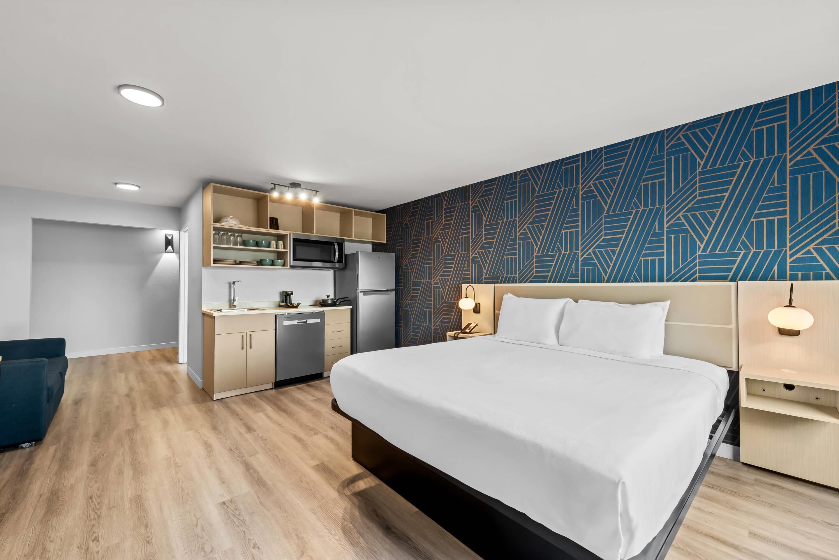 Una habitación de hotel moderna con una cama grande, kitchenette y una pared con diseño.
