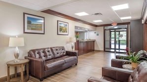 A lobby with a brown leather sofa, a wooden side table, a lamp, framed pictures on the wall, and a reception desk with a potted plant. - Best Western Mason Inn (Mason)