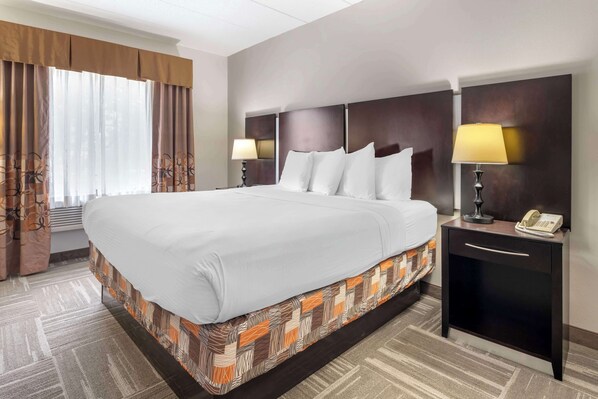 A hotel room with a large bed, two bedside tables with lamps, a dark headboard, and a window with curtains.