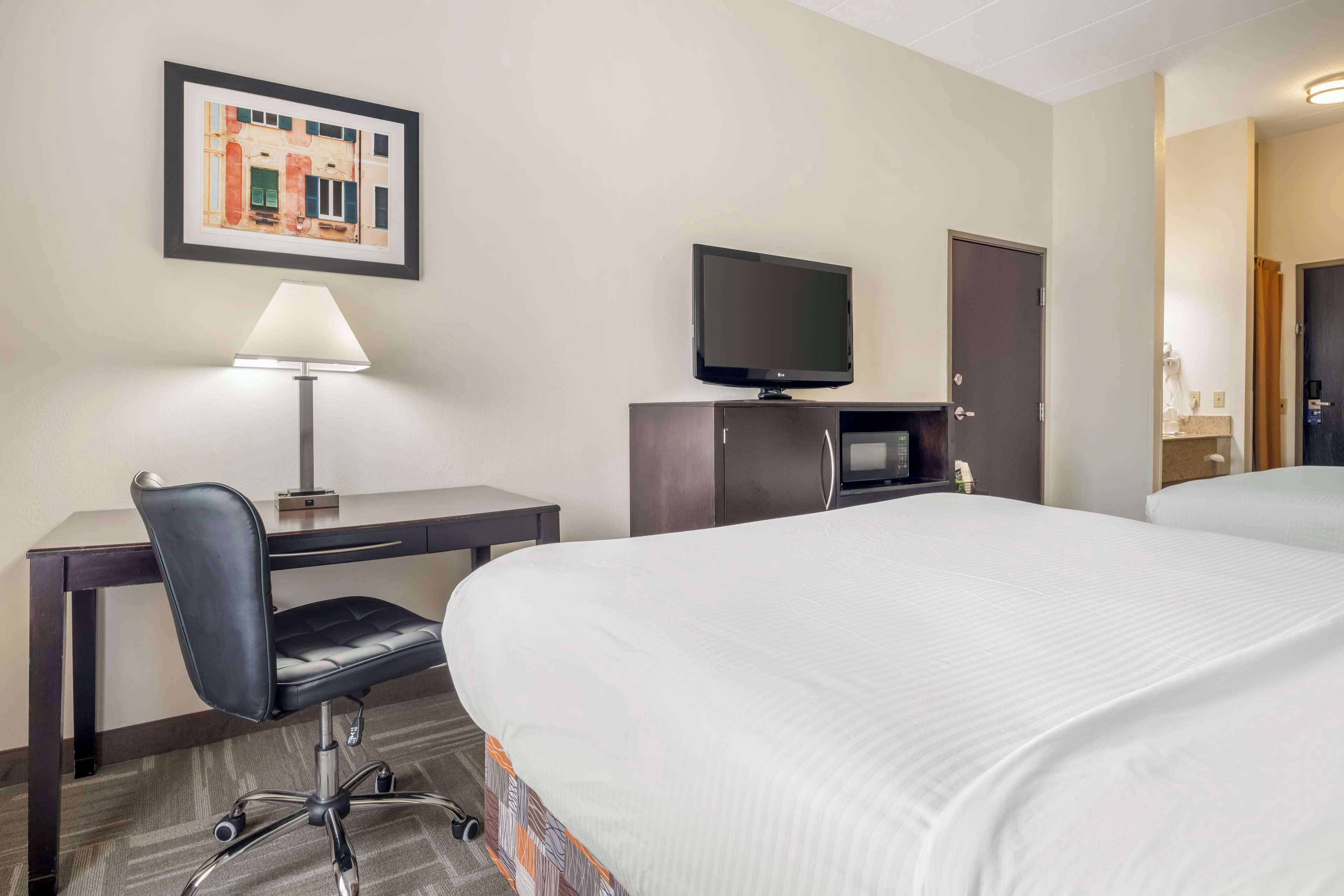 A hotel room with a bed, a desk with a chair, a TV, and a framed picture on the wall.