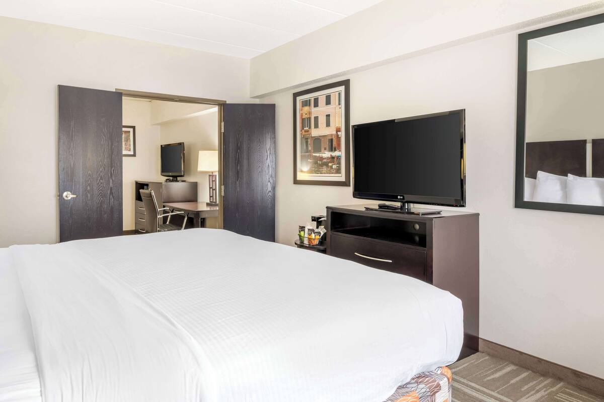 A hotel room with a large bed, a flat-screen TV, a dresser, and a mirror.