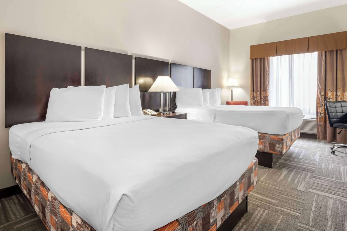 A hotel room with two beds, a desk, a chair, and a large window with curtains.