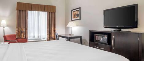 A hotel room with a large bed, a television, a desk with a lamp, a chair, a microwave, and a cabinet.