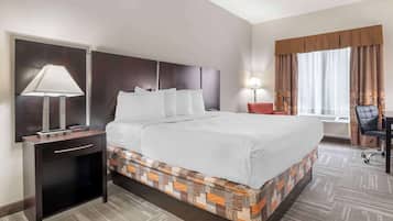 Een hotelkamer met een groot bed, een bureau met stoel, een lamp en een raam met gordijnen.