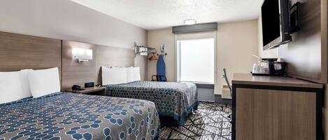 Habitación de hotel con dos camas, un escritorio, un televisor, una ventana y un televisor montado en la pared.