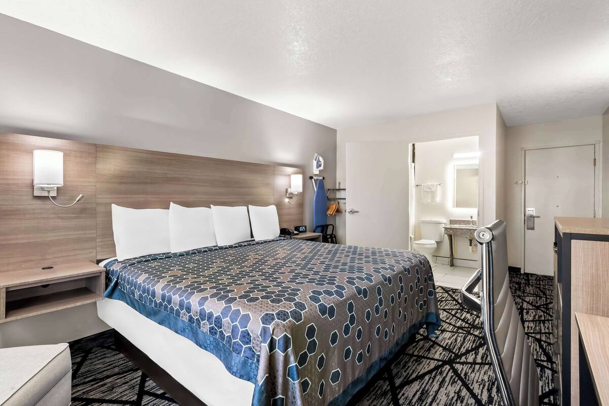 A hotel room with a large bed, bedside tables, a desk, a chair, a bathroom with a toilet and sink, and a shower area.