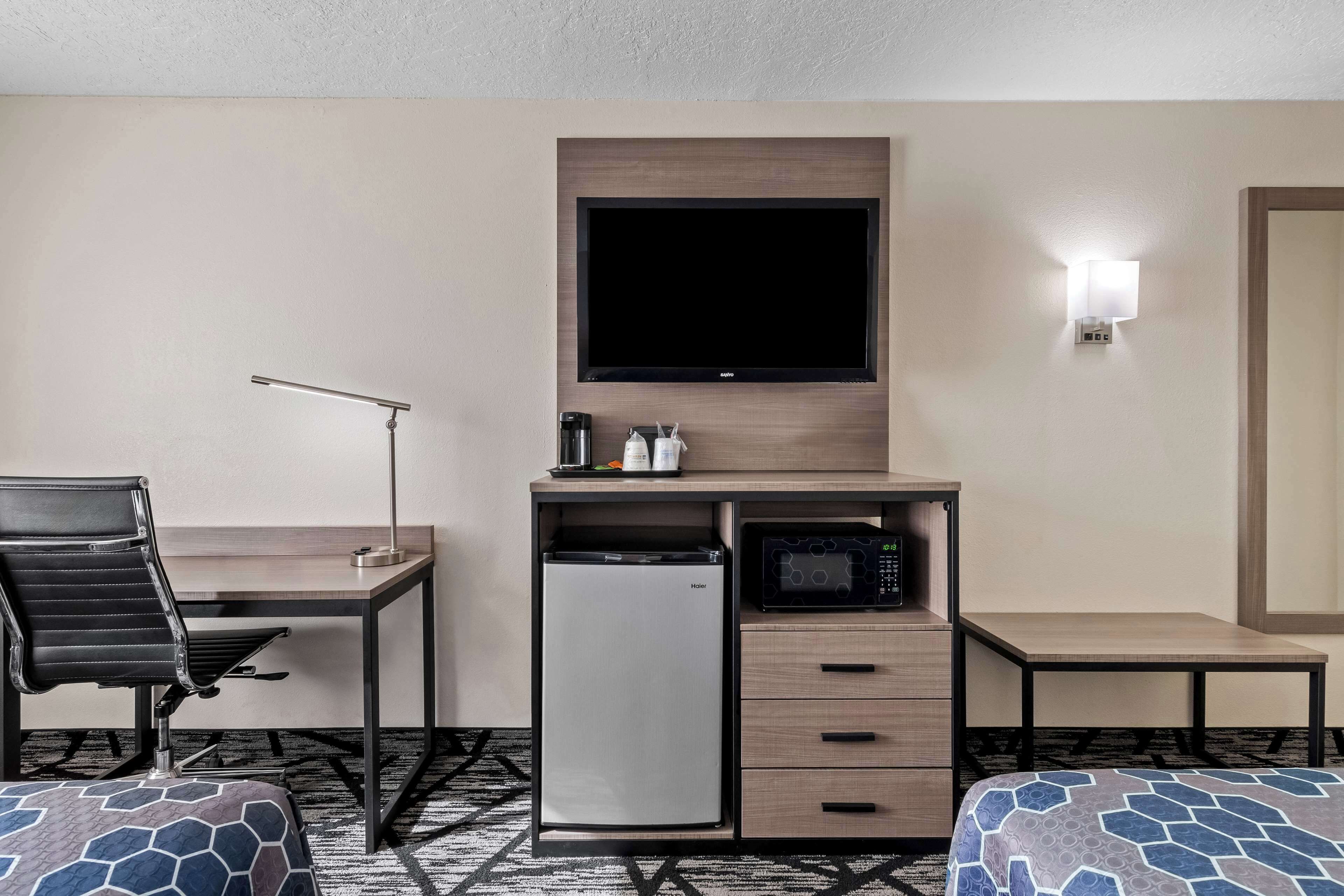 A hotel room with a desk, a television, a microwave, a refrigerator, a chair, and two beds.