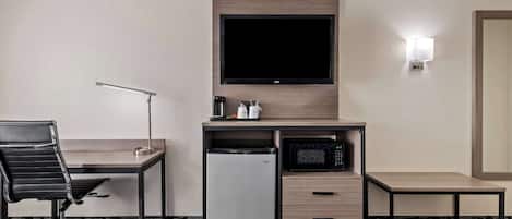 A hotel room with a desk, a television, a microwave, a refrigerator, a chair, and two beds.