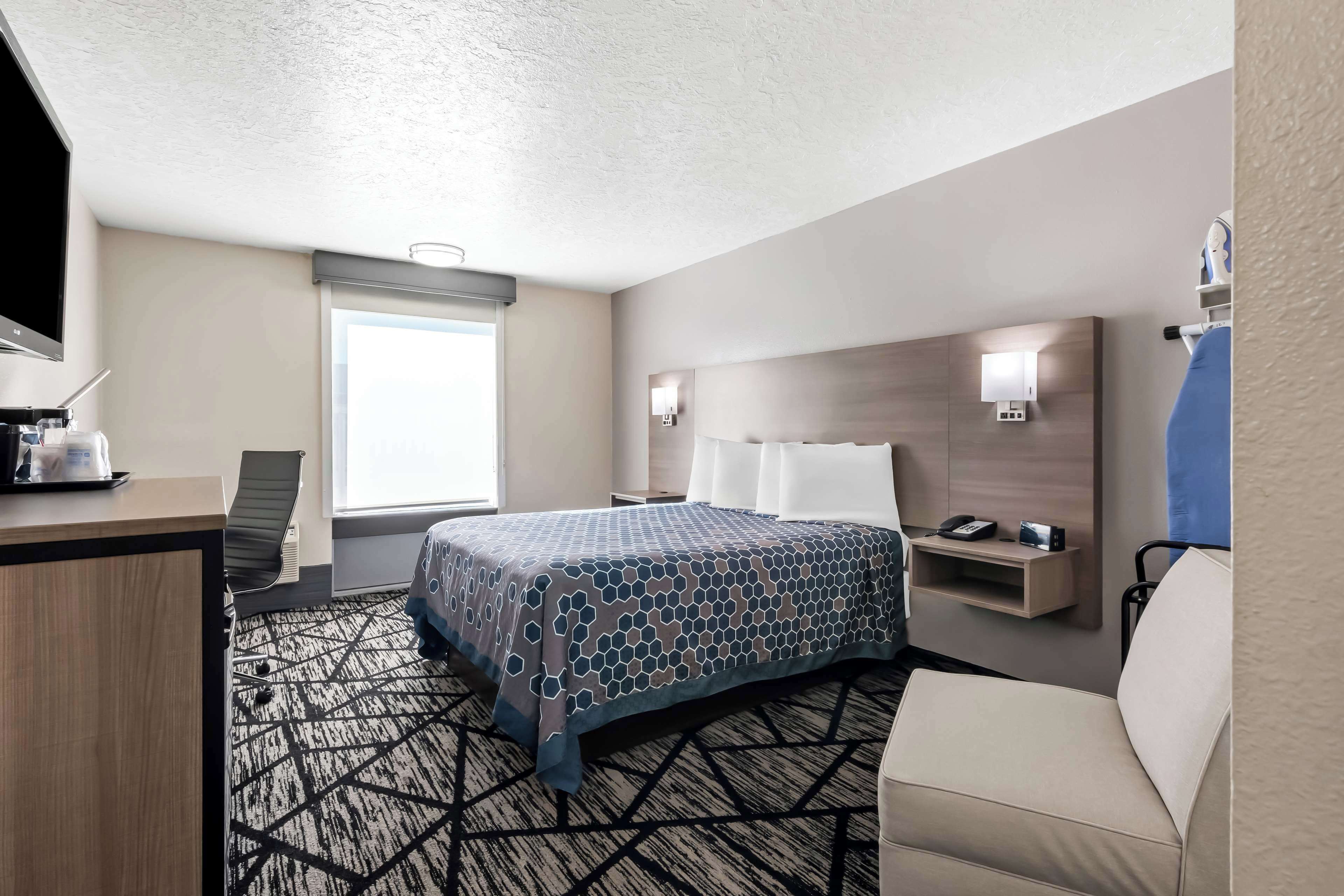 A hotel room with a bed, desk, chair, and a window.