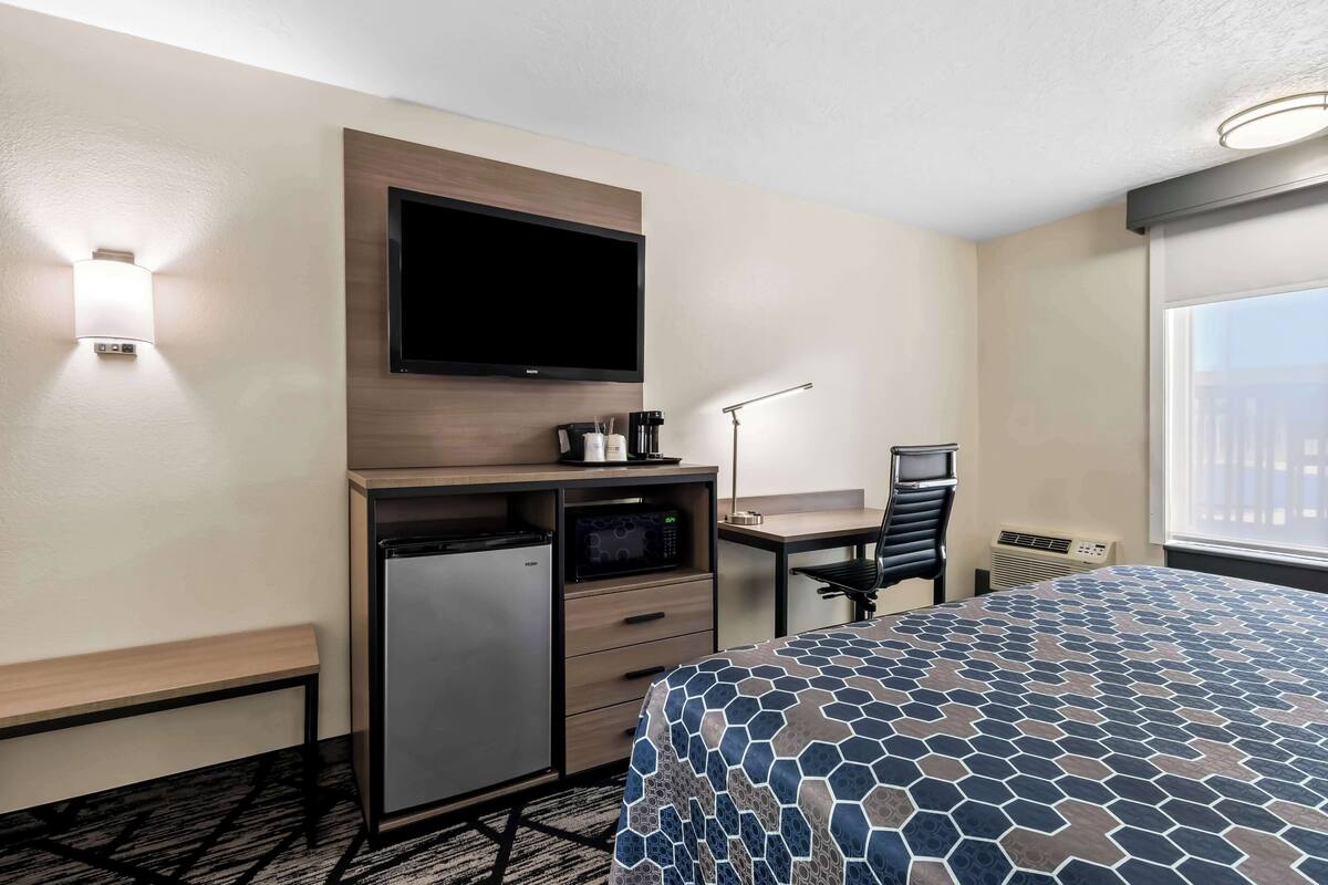 A hotel room with a bed, a desk with a computer, a microwave, a mini fridge, and a TV mounted on the wall.