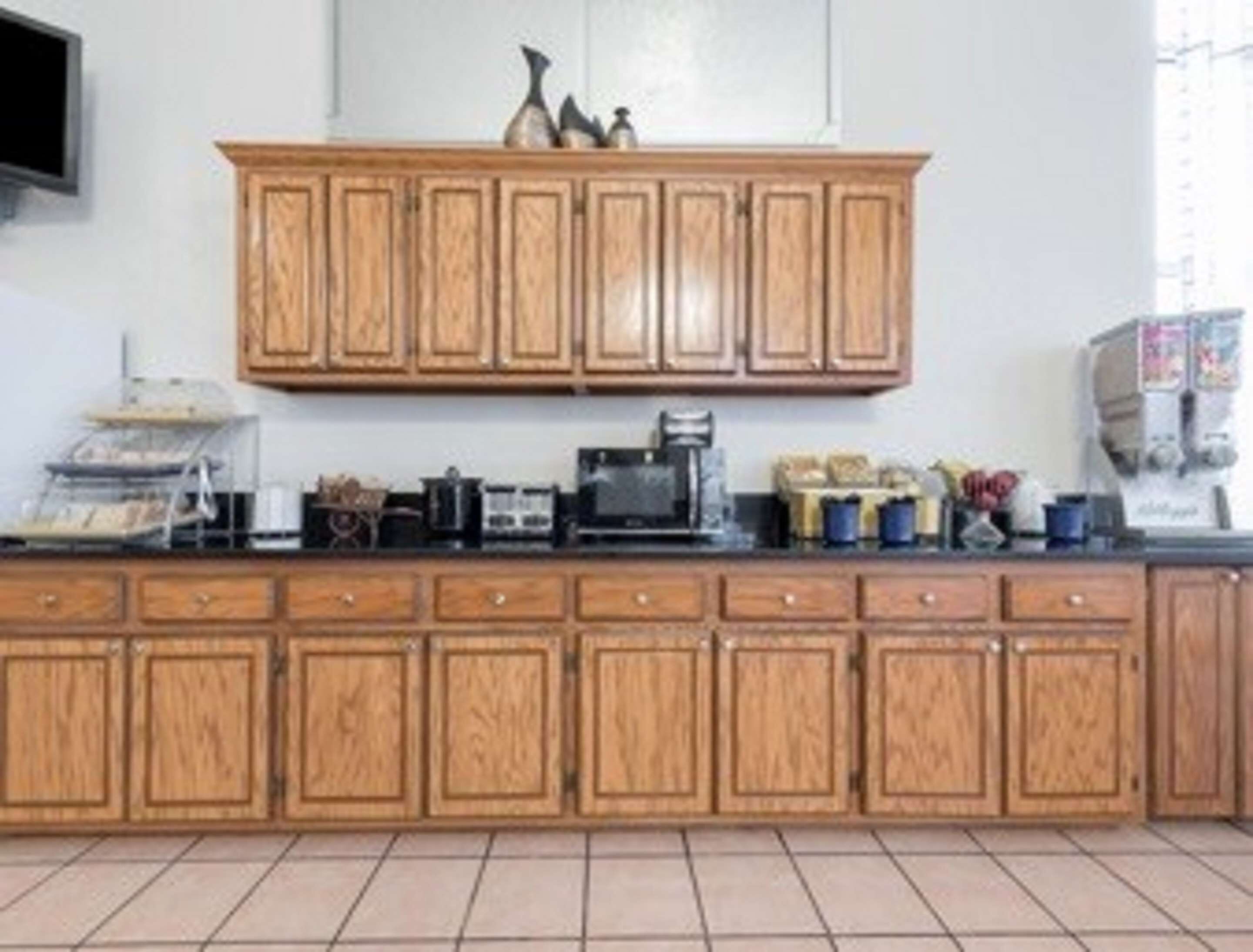 Une cuisine avec des meubles de rangement en bois, un plan de travail équipé de divers appareils et une fenêtre avec des stores.