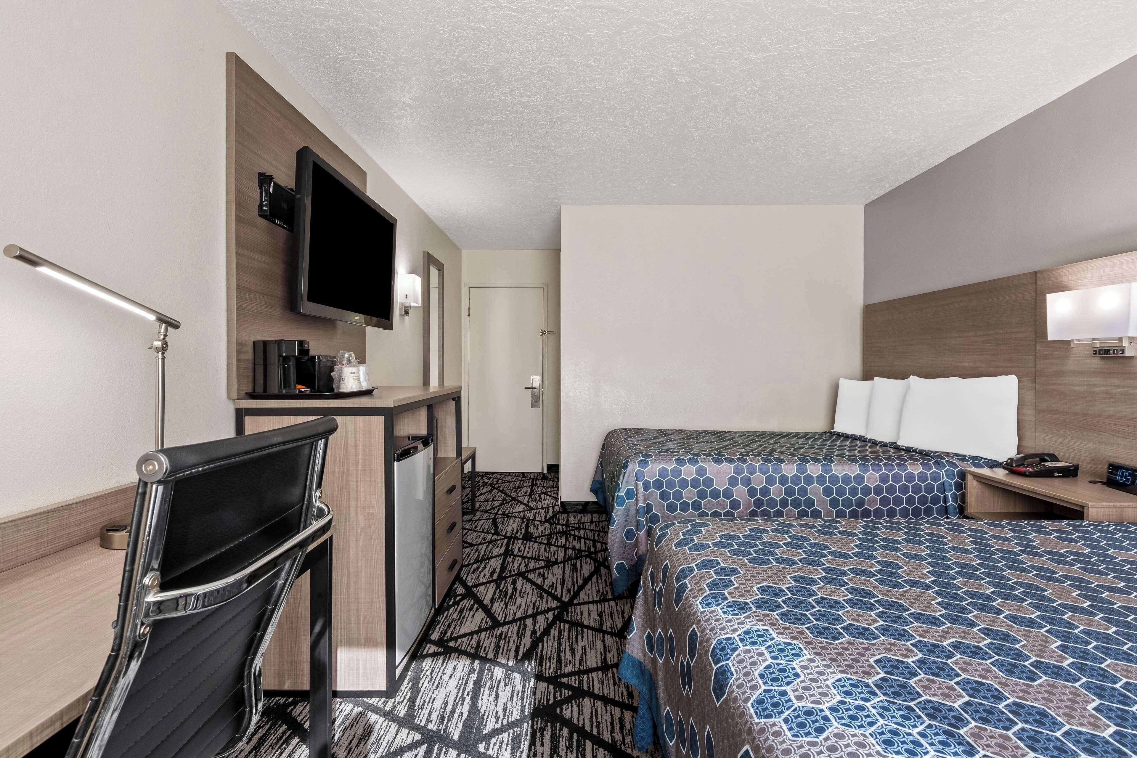 Habitación de hotel con escritorio, silla, cama con ropa de cama estampada, televisor y mesita de noche con lámpara.