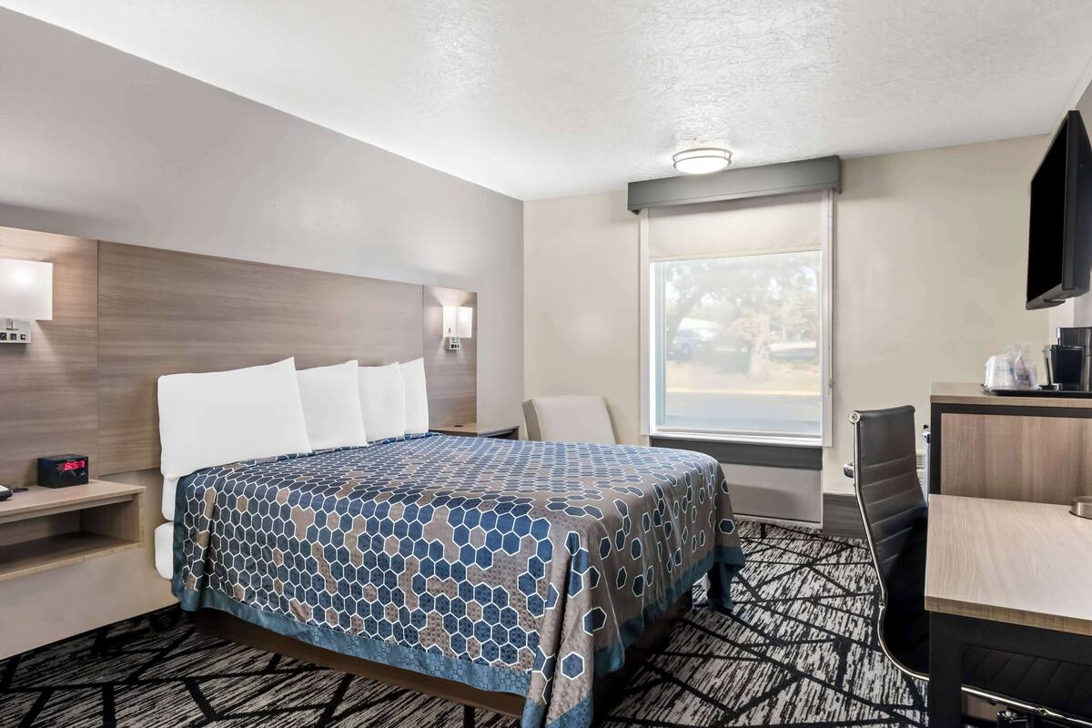 A hotel room with a large bed, a desk, a chair, a TV, and a window with a view of the outside.