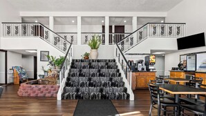 A spacious hotel lobby with a central staircase, a dining area, and a kitchen visible in the background. - SureStay Hotel by Best Western Duncan (Duncan)