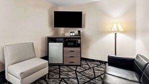 A hotel room with a sofa, a desk with a microwave, a television, and a lamp. - SureStay Hotel by Best Western Duncan (Duncan)