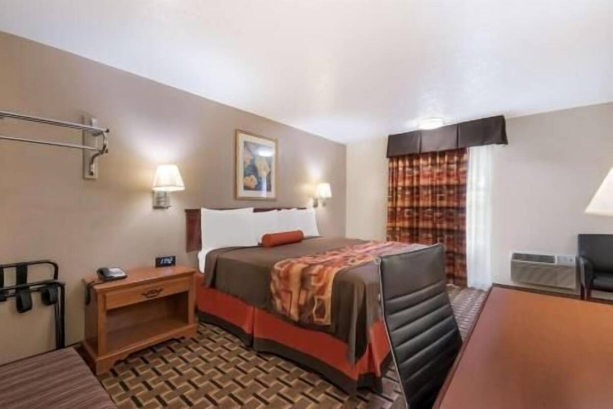 A hotel room with a bed, bedside table, lamp, and a window with curtains.