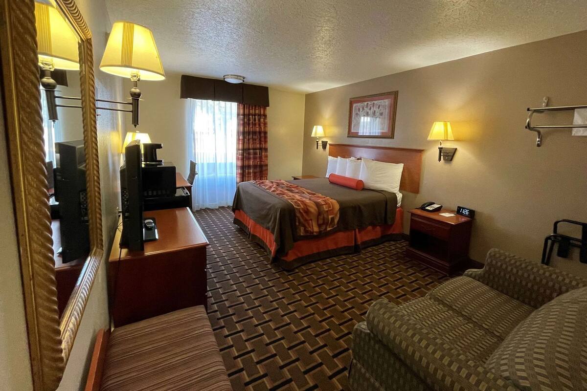A hotel room with a bed, a desk with a computer, a TV, a chair, and a couch.