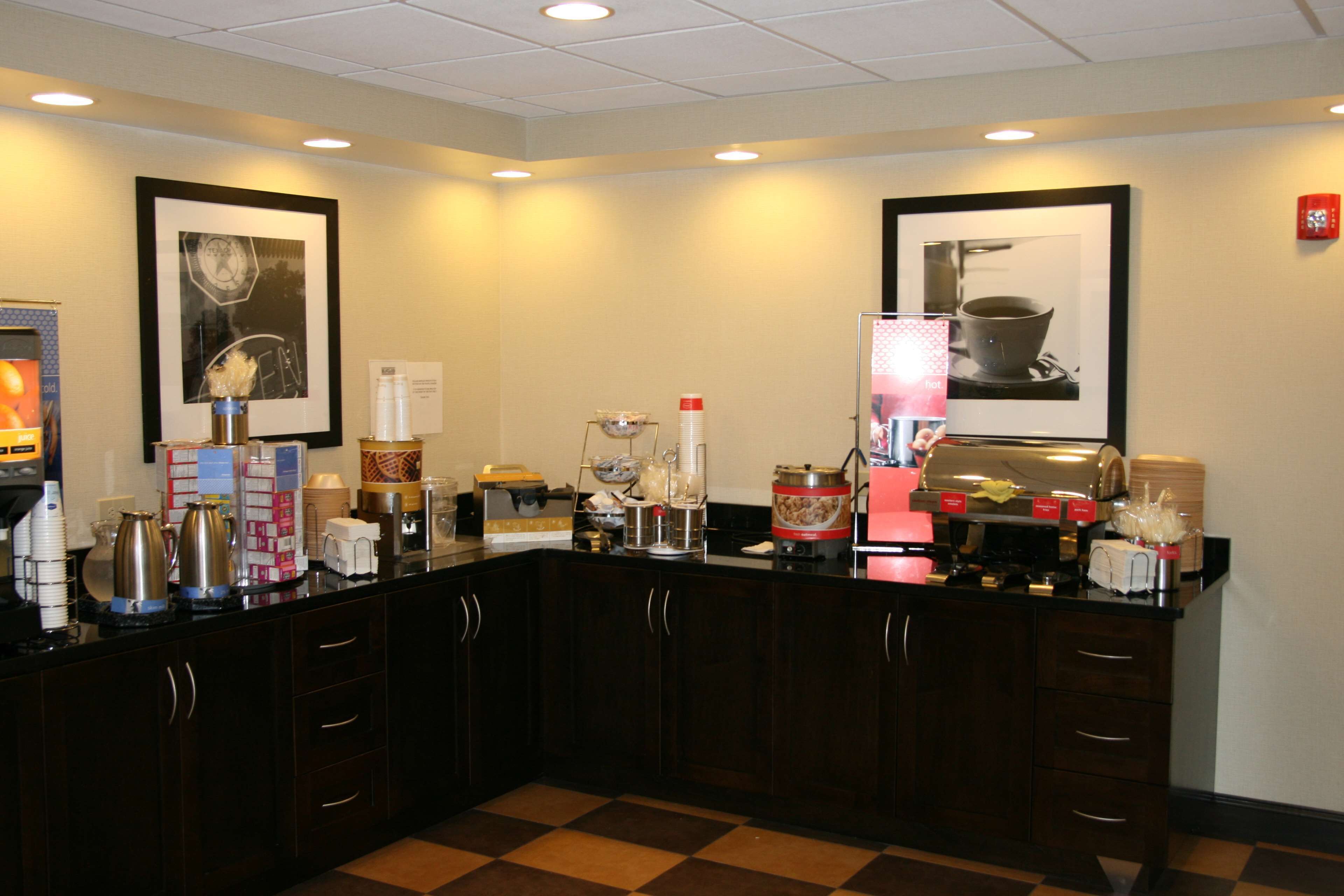 Un espace d’accueil d’hôtel comprenant un comptoir d’enregistrement, des œuvres d’art encadrées aux murs et divers équipements, tels que des machines à café et un distributeur de nourriture.