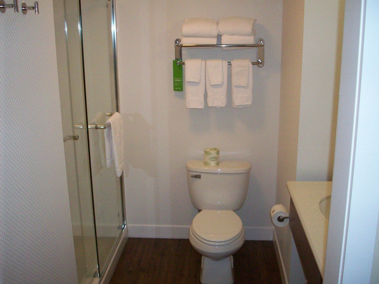 A bathroom with a glass shower enclosure, a toilet with a paper towel holder, and a towel rack with folded towels.