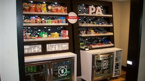Ein Automatenbereich mit verschiedenen Snacks und Getränken, inklusive einer Durchsagemelanlage-Beschilderung über den Regalen.