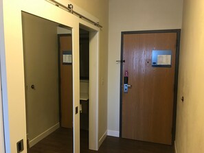 A hallway with a wooden door on the right, a white door on the left, and a closet with a mirror and a bulletin board. - Hampton Inn Uniontown (Uniontown)