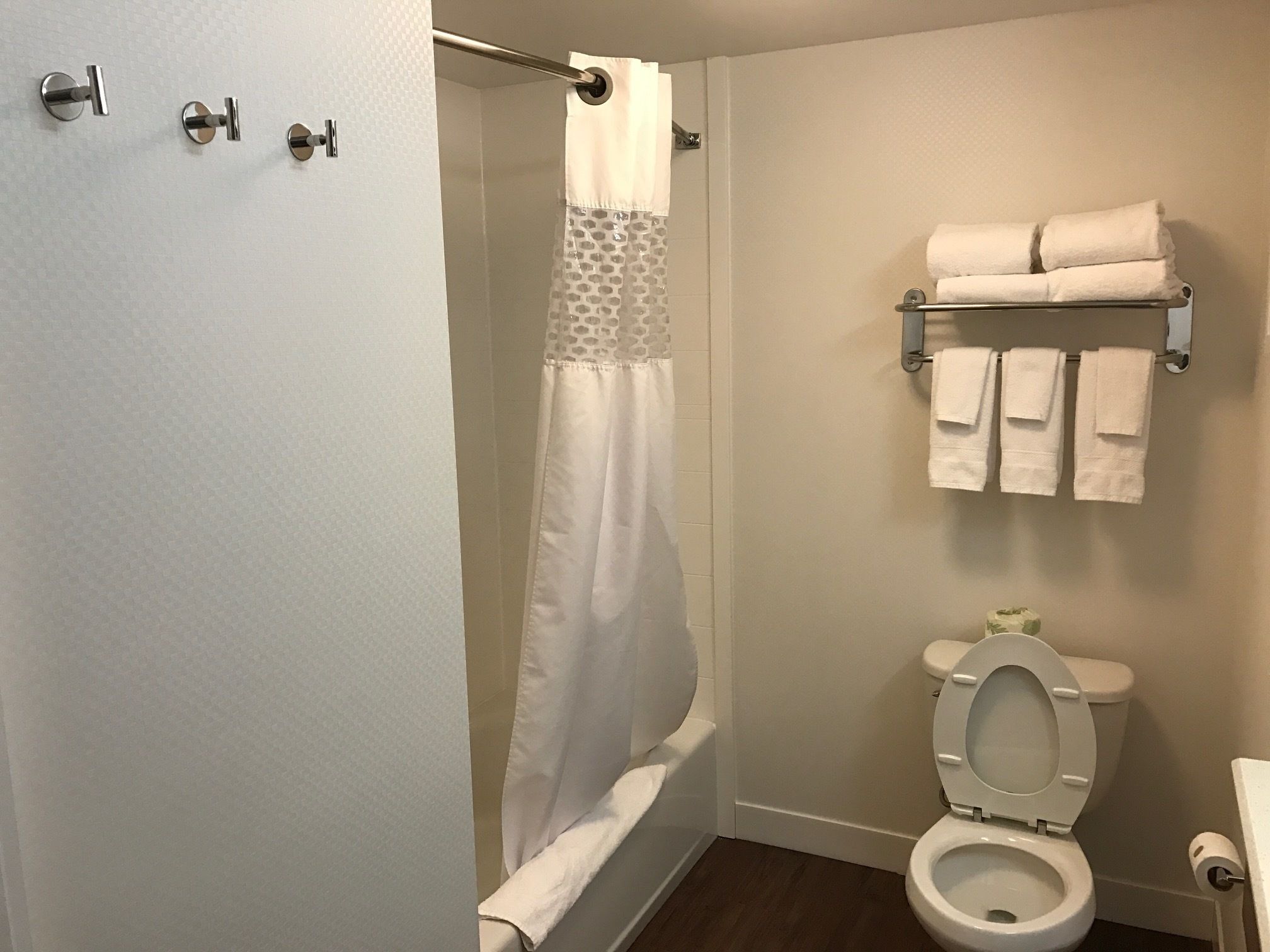 A bathroom with a shower curtain, a toilet, and a towel rack with towels.