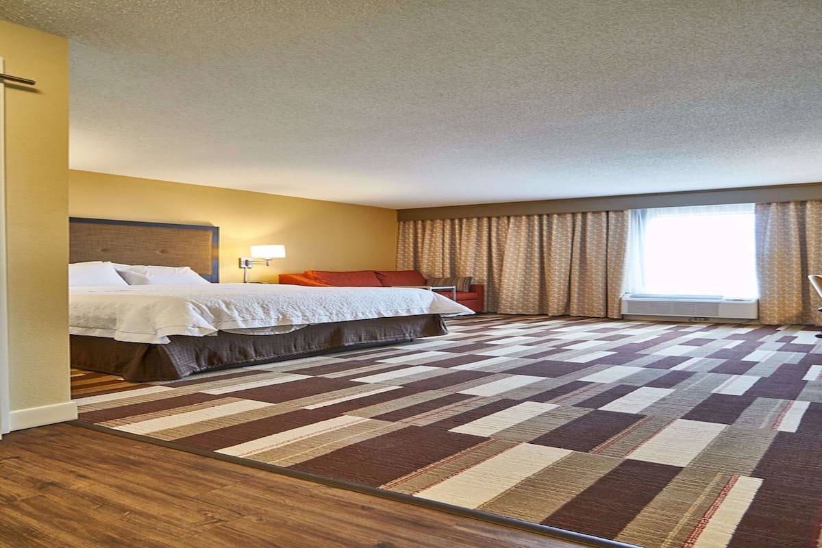 Una habitación de hotel con una cama grande, un escritorio y un ventanal con cortinas.