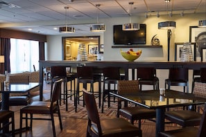 Un hall de hotel con una zona de bar, arreglos de asientos y un televisor montado en la pared.