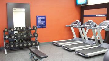 Un gimnasio con cintas de correr, mancuernas y un banco.