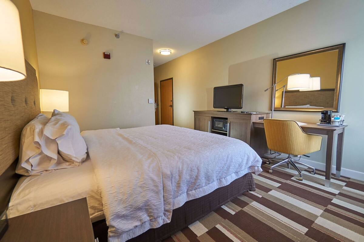 Une chambre d’hôtel équipée d’un lit, d’un bureau avec un ordinateur, d’une chaise, d’une télévision et d’un miroir.