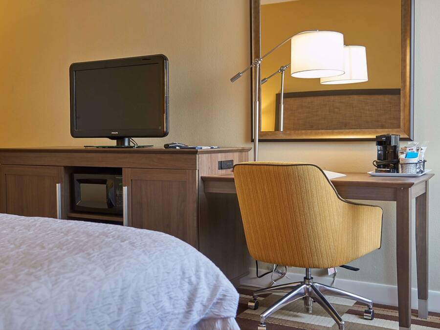 Een hotelkamer met een bed, een bureau met een computer, een stoel, een lamp en een koffiezetapparaat.
