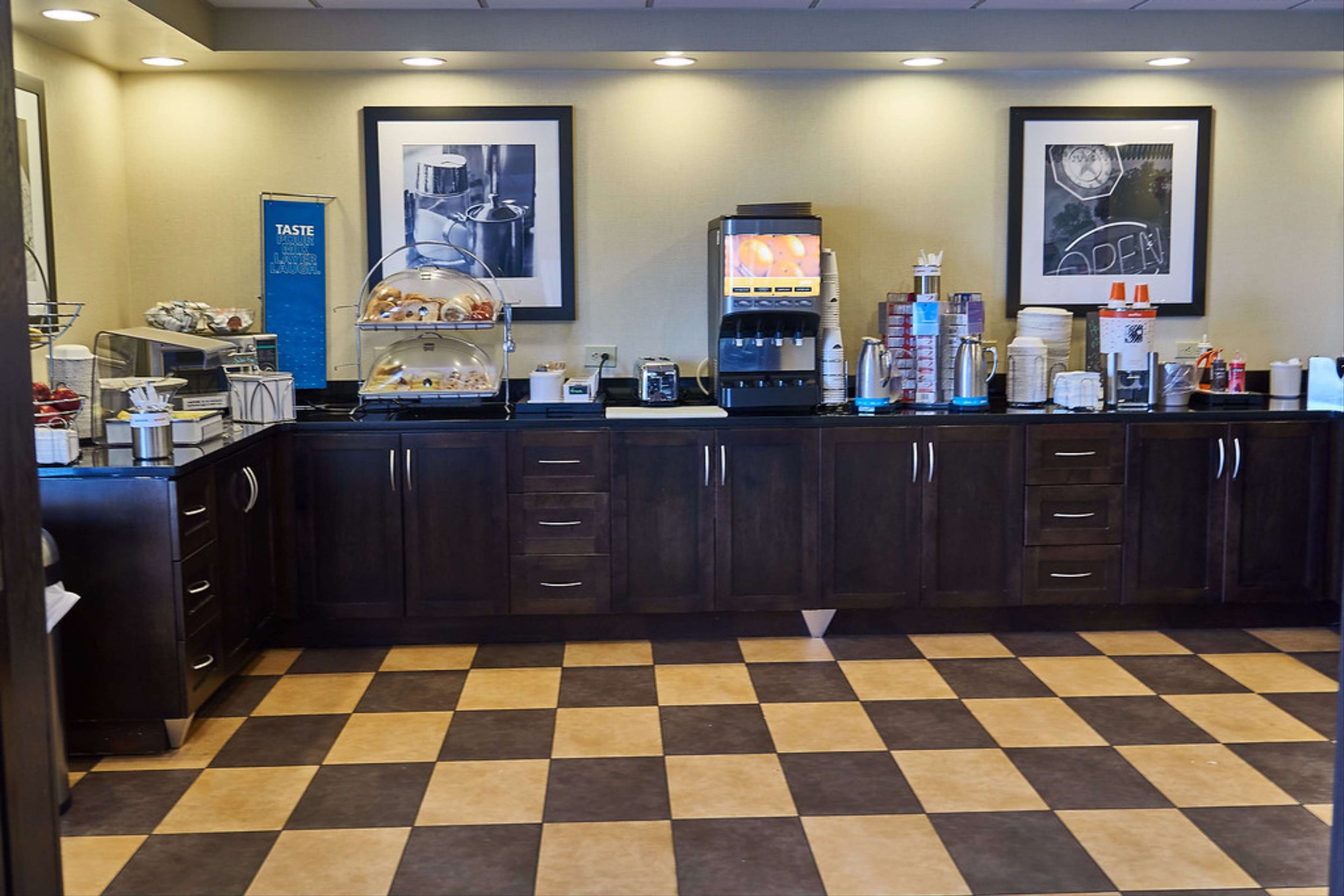 Zona de recepción de un hotel con suelo a cuadros, una máquina de café, una vitrina de comida y cuadros en la pared.
