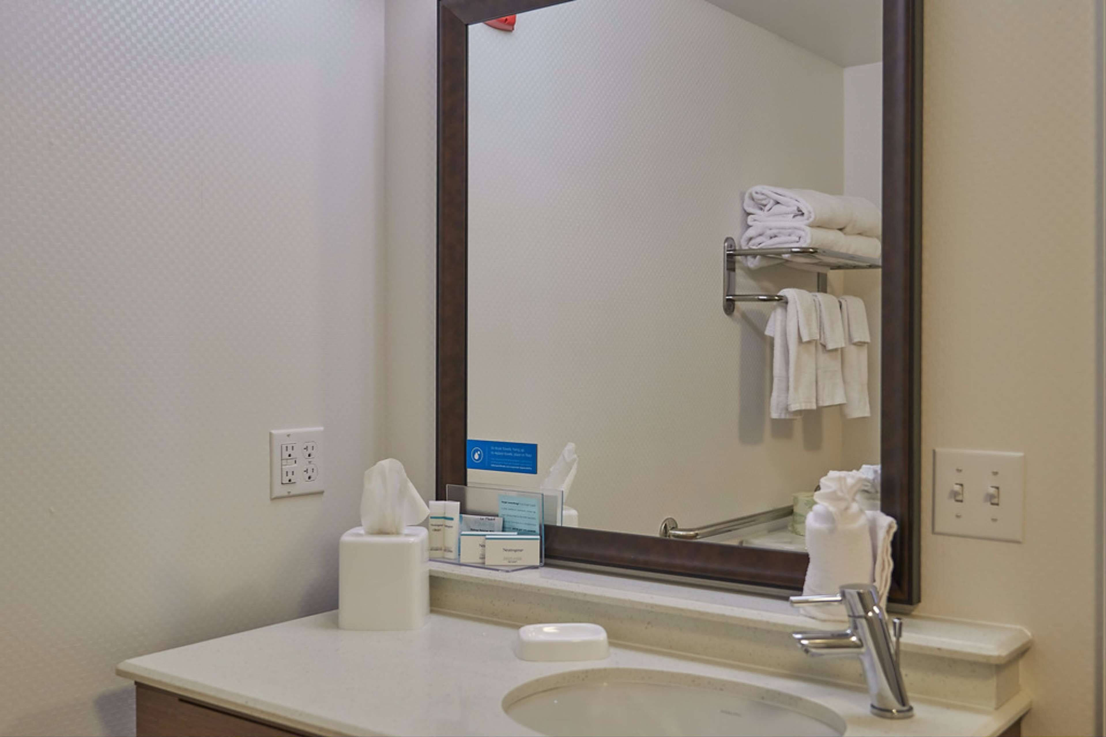 A hotel bathroom with a sink, mirror, and towel rack.