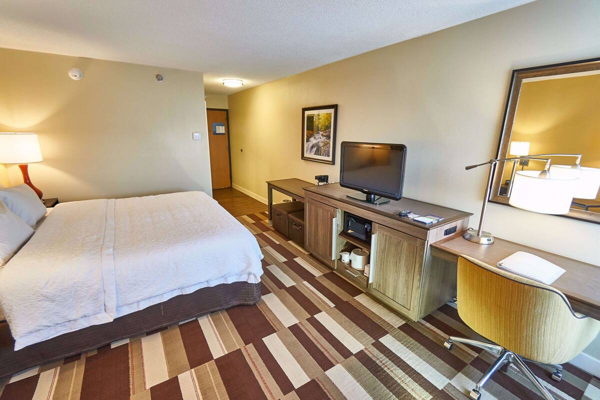 Habitación de hotel con cama, escritorio con computadora, televisor y espejo de baño.