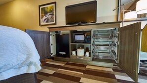 Ein Hotelzimmer mit einem Bett, einem an der Wand montierten Fernseher, einer Mikrowelle und einem kleinen Kühlschrank.