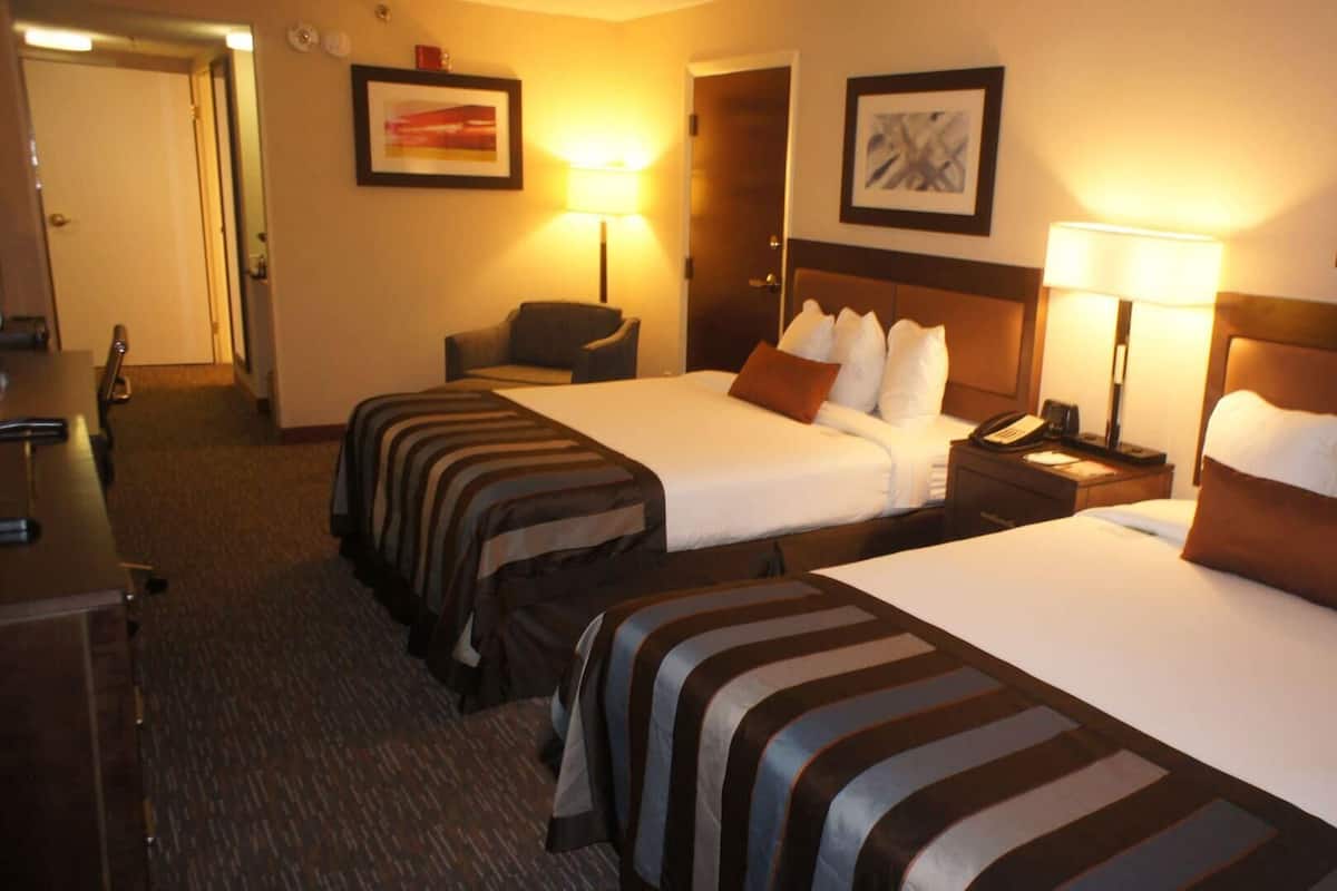 Quarto de hotel com duas camas, uma escrivaninha, uma cadeira e duas luminárias de cabeceira.
