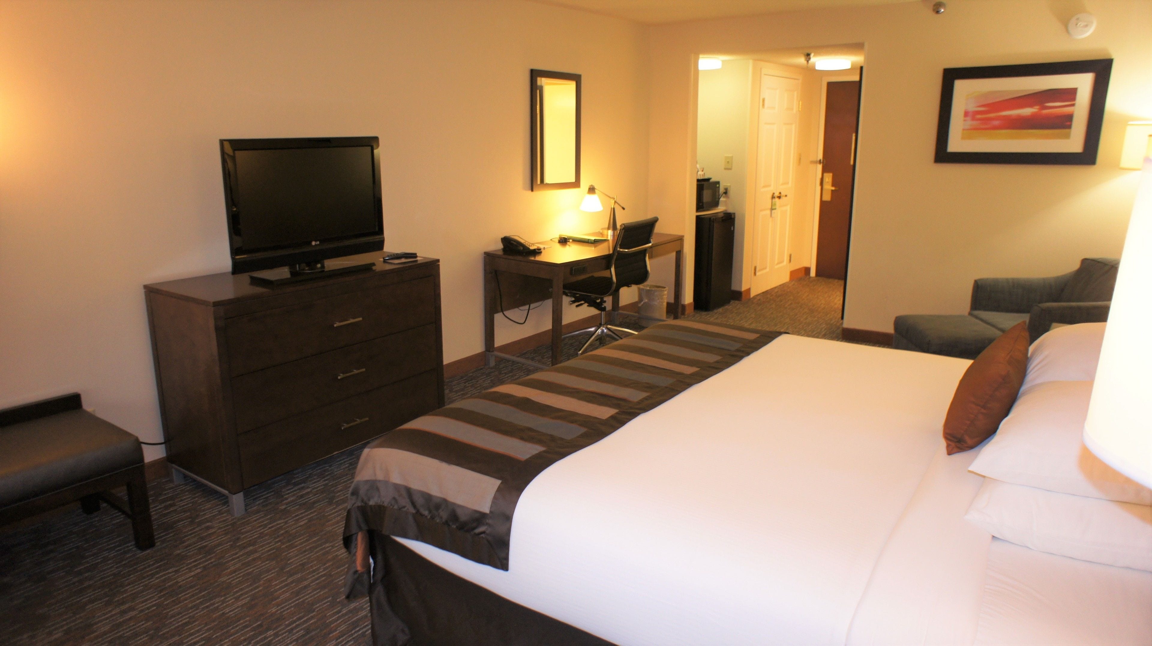 A hotel room with a bed, a desk, a television, a chair, and a door leading to a bathroom.