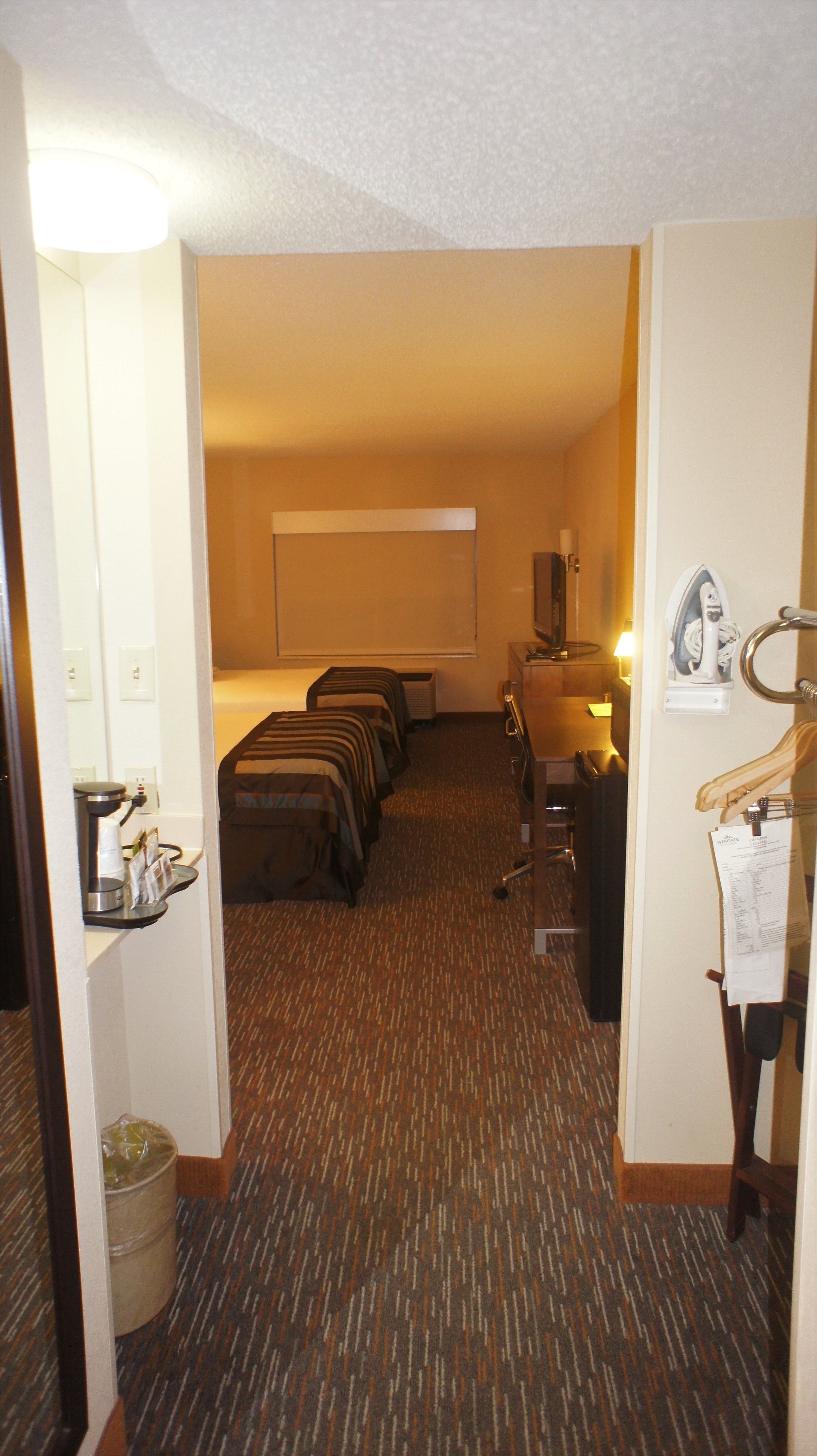 A hotel room with a bed, a desk, a chair, a mirror, and a coat rack.