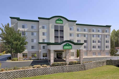 A multi-story hotel with a green and white facade, a central entrance with a sign, and a stone retaining wall in front.